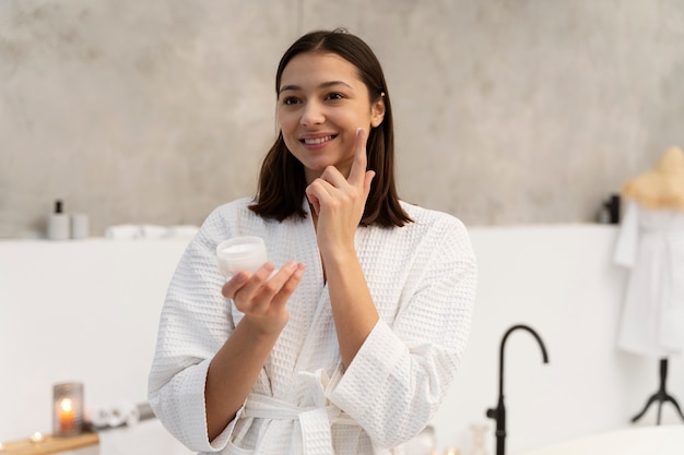 Young woman applying moisturizer on her face before taking a bath