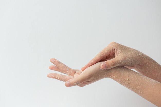 Young woman applying natural lemon scrub on hands against white surface