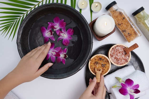 Free photo young woman applying natural scrub on hands against white surface. spa treatment and product for female hand spa, massage, perfumed flowers water and candles, relaxation. flat lay. top view.