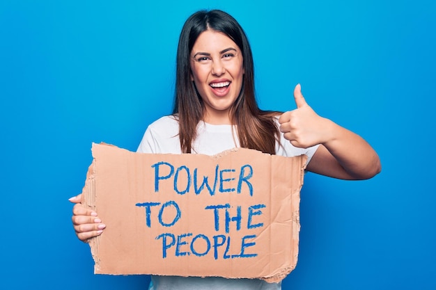 Free photo young woman asking for social movement holding banner with power to the people message smiling happy and positive thumb up doing excellent and approval sign