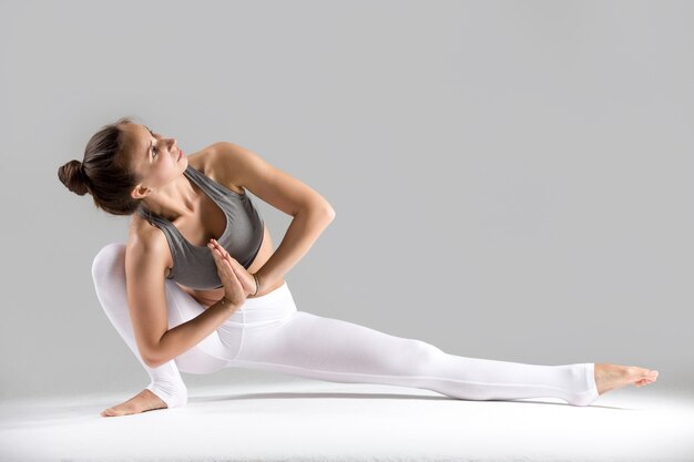 Young woman in Baddha Ardha Samakonasana pose, grey studio background