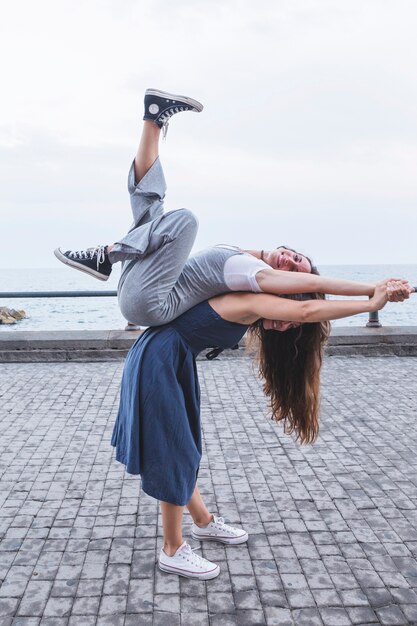 Young woman balancing friend on her back standing near the sea