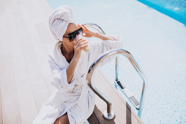 Free photo young woman in bathrobe drinking coffee by the pool