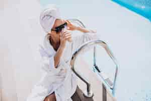 Free photo young woman in bathrobe drinking coffee by the pool