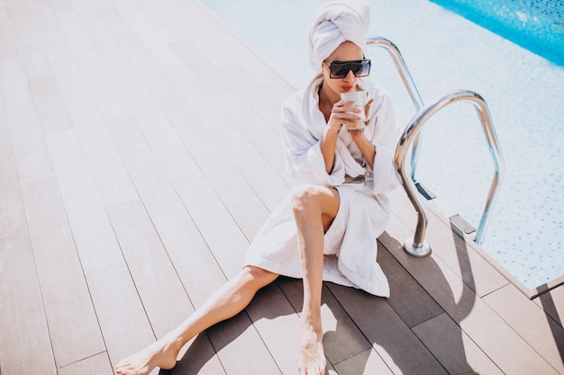 Young woman in bathrobe drinking coffee by the pool