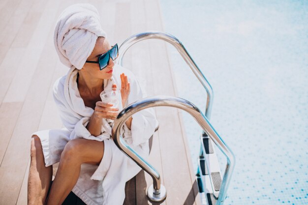 Young woman in bathrobe drinking coffee by the pool