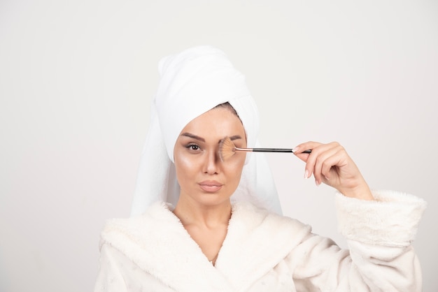 Young woman in a bathrobe holding make-up brush