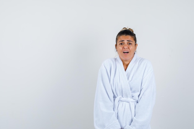 Free photo young woman in bathrobe shrugging and looking amazed