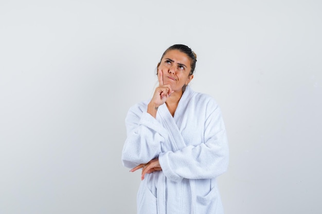 Young woman in bathrobe standing in thinking pose and looking thoughtful