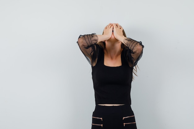 Free Photo young woman in black blouse and black pants covering face with hands and looking regretful 