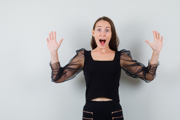 Young woman in black blouse raising hands as winner and looking happy 