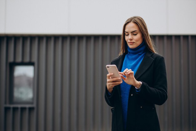 Young woman in black coat using phone