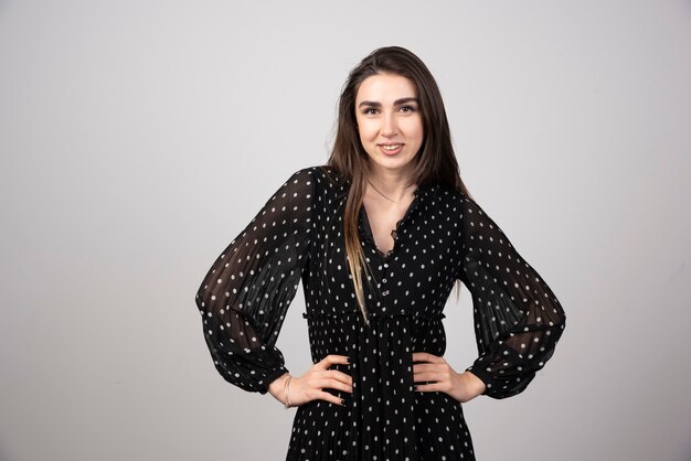 Young woman in black dress posing on gray.