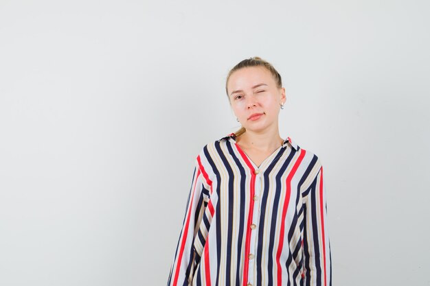 Young woman blinking and posing in striped blouse and looking confident