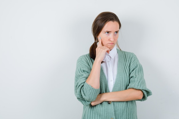 Young woman in blouse, cardigan thinking about something, looking away and looking gloomy , front view.