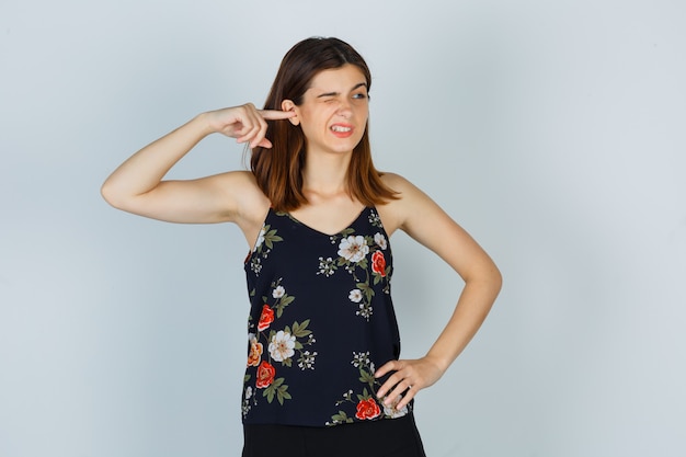 Free photo young woman in blouse plugging ear with finger and looking confused , front view.