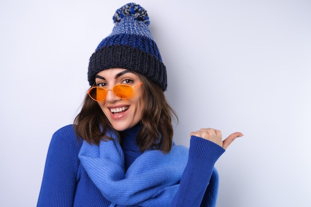 Young woman in a blue golf turtleneck hat and scarf sunglasses on a white background cheerful in a good mood