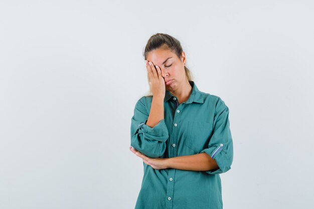 Young woman in blue shirt leaning at her hand and looking sleepy