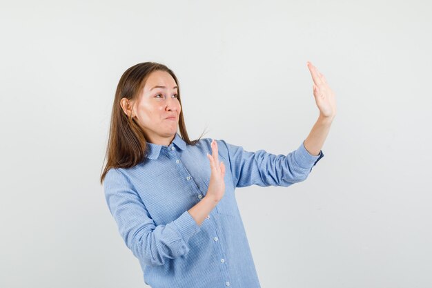 Young woman in blue shirt raising hands in preventive manner