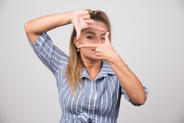 Free photo young woman in blue sweater taking photo with her hand.