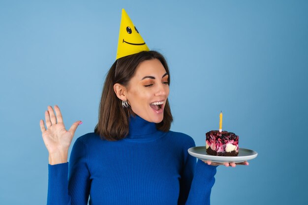 Free photo young woman on a blue wall celebrates a birthday, holds a piece of cake, in a great mood, happy, excited