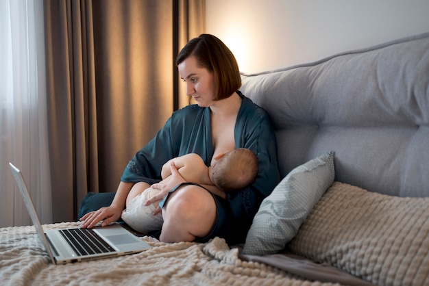 Young woman breastfeeding her cute baby while working