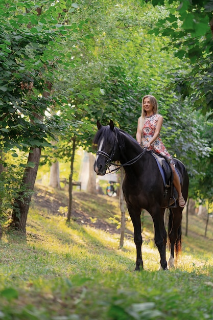 Young woman in a bright colorful dress riding a black horse