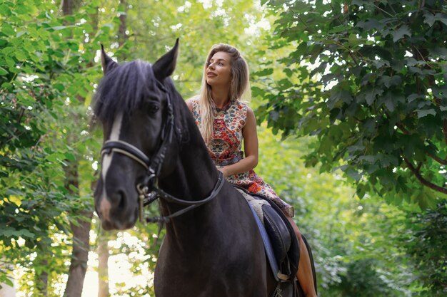 Young woman in a bright colorful dress riding a black horse