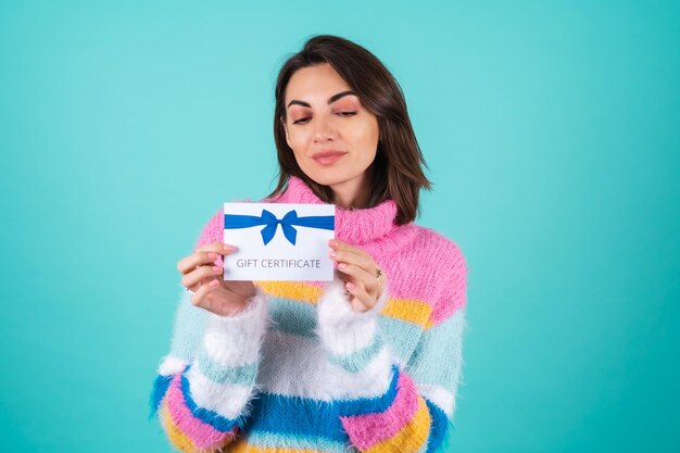 Young woman in a bright multicolored sweater on blue holding a gift certificate