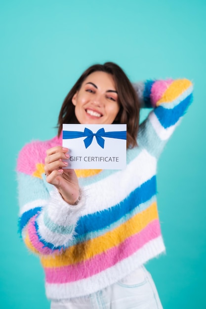 Young woman in a bright multicolored sweater on blue holding a gift certificate