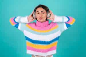 Free photo young woman in a bright multicolored sweater on blue in large noise canceling headphones