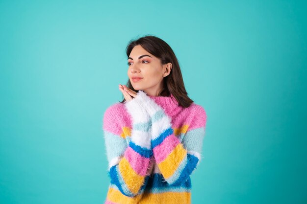 A young woman in a bright multicolored sweater on blue smiles cutely