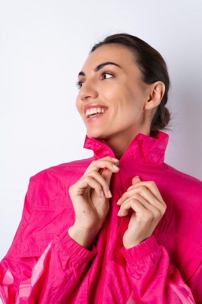 A young woman in a bright pink sports jacket on a white background smiles cheerfully vertical frame