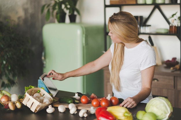 Young woman browsing on digital tablet while preparing food