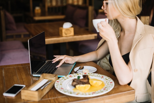 Free photo young woman browsing laptop while having breakfast in the caf���