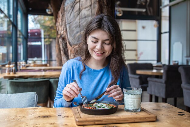 A young woman in a cafe dines on traditional shakshuka and ayran