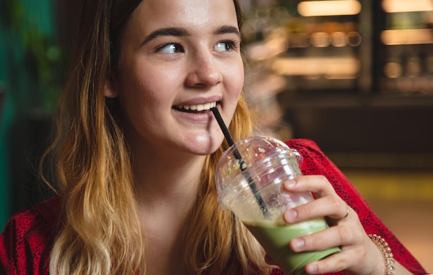 A young woman in a cafe drinks a green drink ice latte