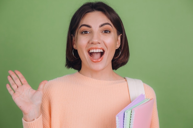 Young woman in casual peach sweater and backpack isolated on green olive color wall