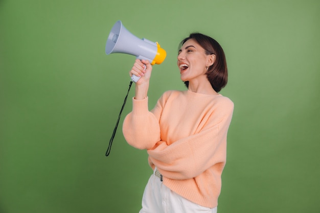 Young woman in casual peach sweater isolated on green olive color wall