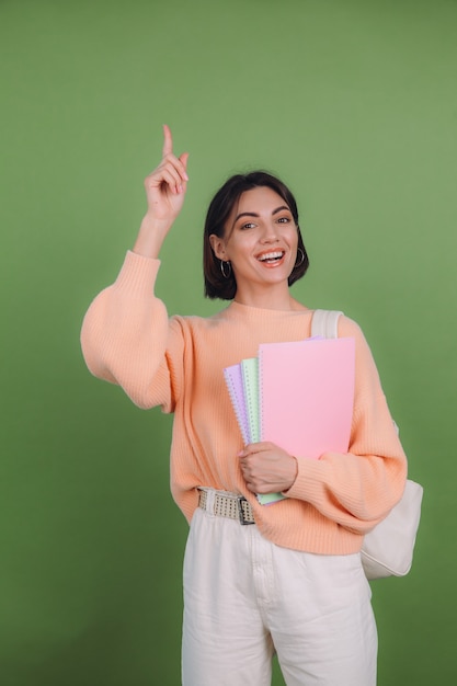 Young woman in casual peach sweater isolated on green olive color wall