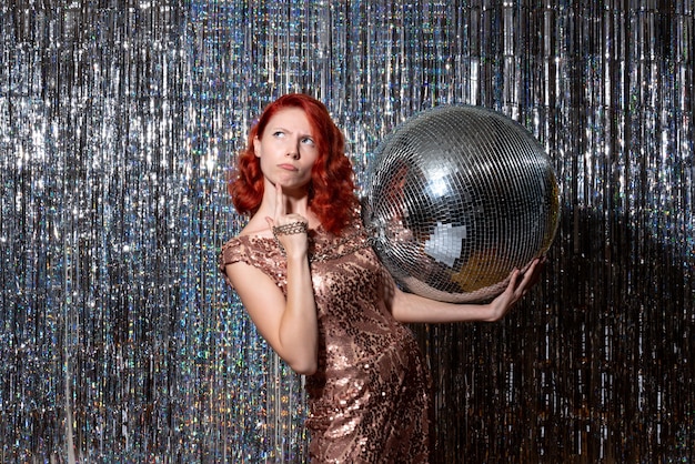 young woman celebrating new year in party holding disco ball on bright curtains curtains