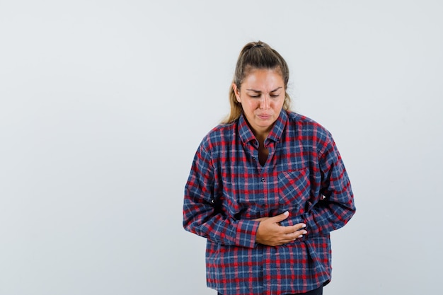 Young woman in checked shirt having bellyache and looking exhausted