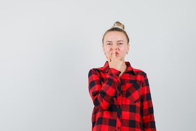 Free Photo young woman in checked shirt touching her nose with finger and looking cute