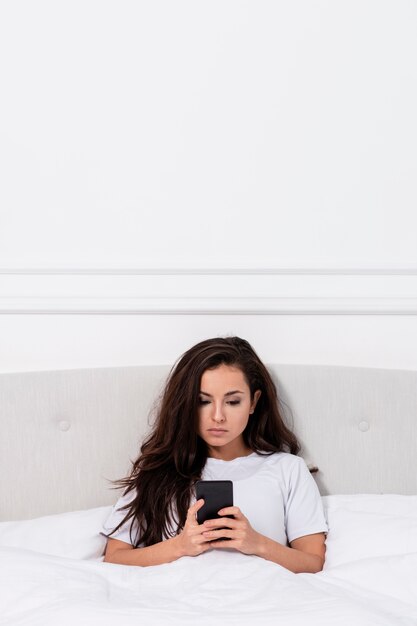 Young woman checking her phone in bed