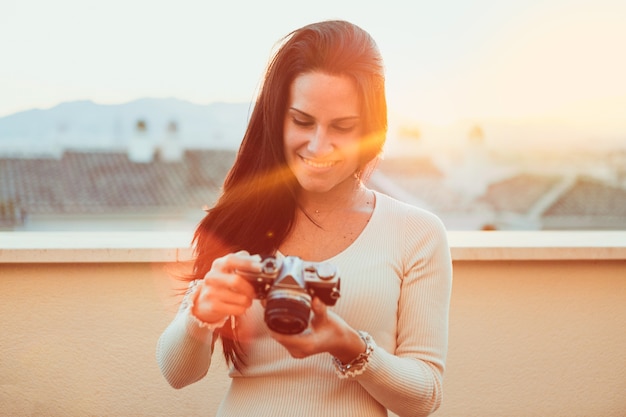 Free Photo young woman checking her vintage camera at sunset