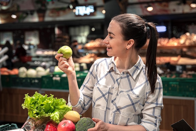 Free photo a young woman chooses fruits and vegetables in a supermarket