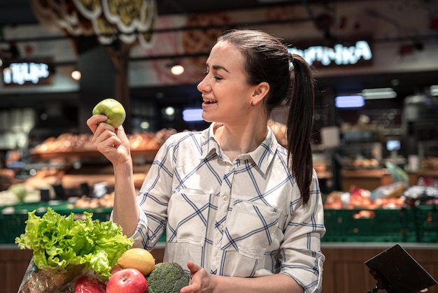 A young woman chooses fruits and vegetables in a supermarket