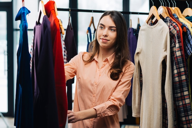 Young woman choosing dresses in store