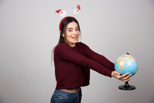 Young woman in Christmas headband holding an Earth globe.