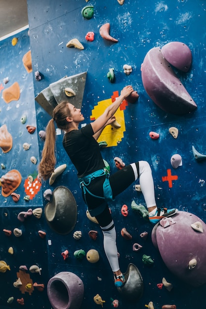 Young woman climbing a tall, indoor, man-made rock climbing wall